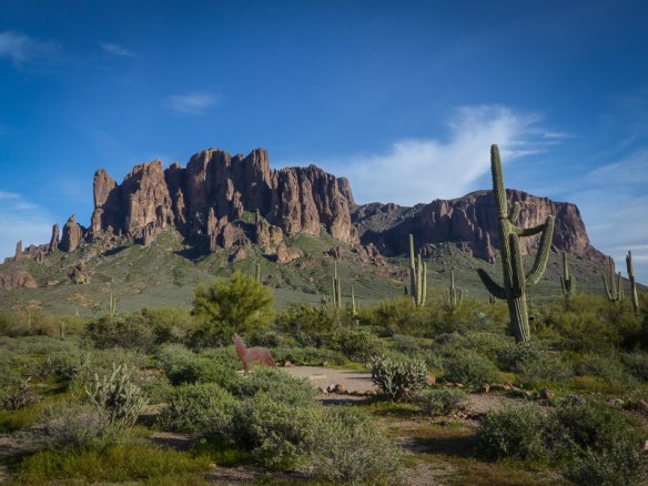 A view of the Superstition Mountains at Lost Dutchman State Park with a coyote sundial and saguaro cactus