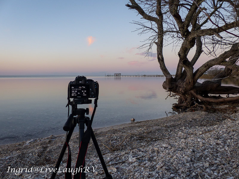 A camera on a beach photography a dock at sunset