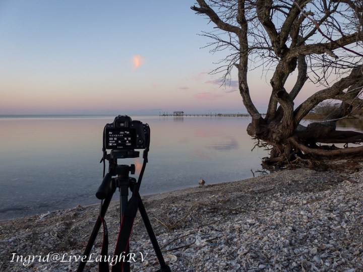 A camera on a beach photography a dock at sunset